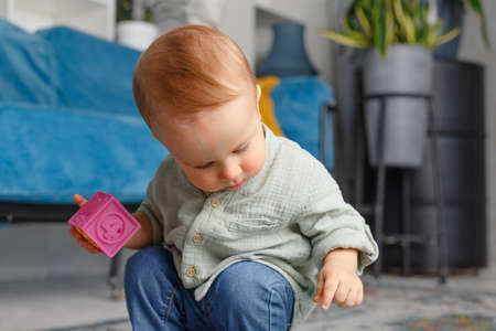 One-year-old baby in jeans and shirt plays with cubes in the apartmentの写真素材