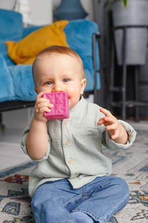 One-year-old baby in jeans and shirt plays with cubes in the apartment