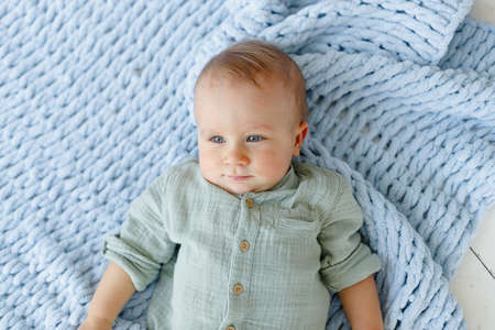 one-year-old blue-eyed baby in a shirt lies on a blanket