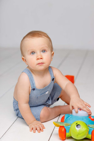 Toddler with blue eyes plays toys sitting on the floor, boy 1 year oldの写真素材
