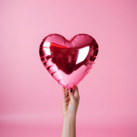 Pink foil heart shaped balloon in a hand on pink background. St Valentines day symbolの素材