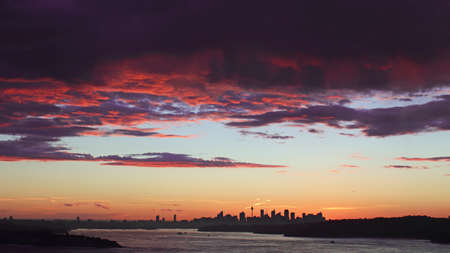 An intense red color of clouds during sunset with Sydney cityscape on the background.の写真素材