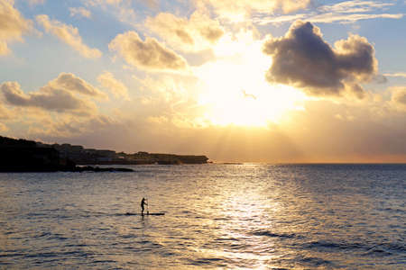 A silhouette of man doing paddle boarding in the golden morning lightの写真素材