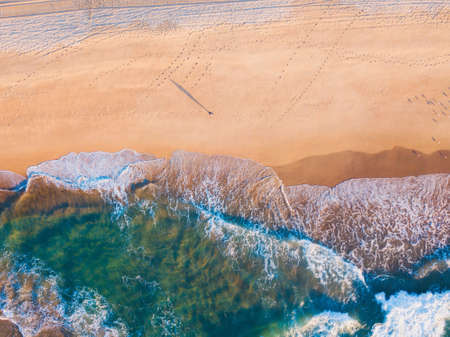 Aerial view of one person standing in the beach with a long shadow.