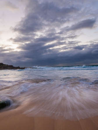 Wave flow between rocks and sand in a cloudy day.の写真素材