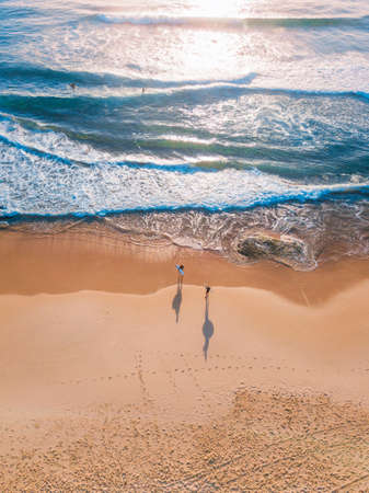 Aerial view of two surfers in the sand about to get into the water.