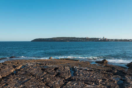 Coastal rock by the ocean during the day with clear blue sky.の写真素材
