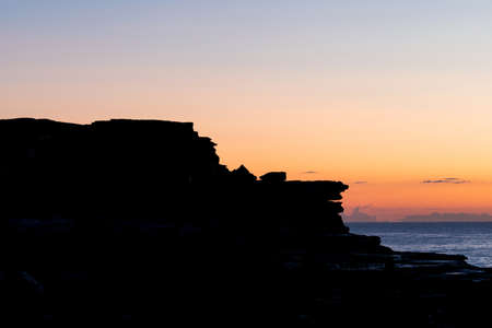 Silhouette of rock cliff with orange sunrise sky.の写真素材