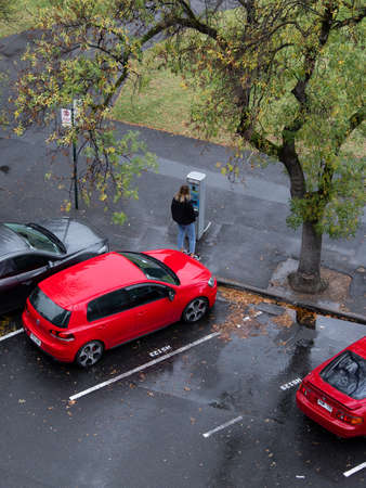 Adelaide, Australia - May 11, 2019: A woman paying for parking ticket in the rain.のeditorial素材
