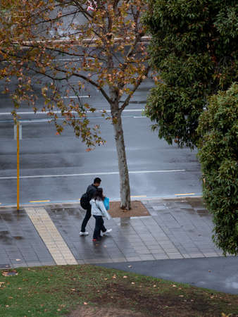 Adelaide, Australia - May 11, 2019: Two people walking on the footpath after rain.のeditorial素材