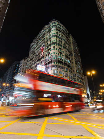 Hong Kong - October 3, 2019: Red bus passing through New Lucky House building at night.のeditorial素材