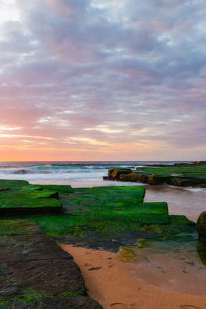 Colorful clouds over mossy rocks and beach at Turimetta Beach, Sydney.の写真素材