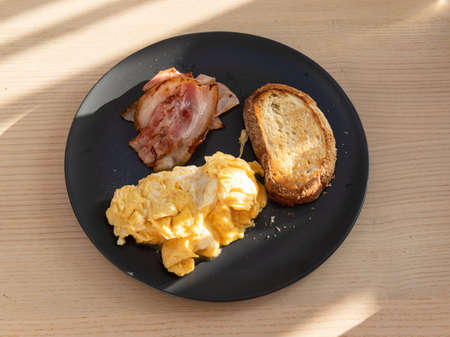 Breakfast plate consists of bread, bacon, and scrambled eggs.の写真素材