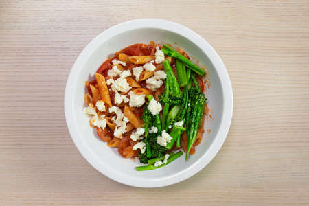 A bowl of tomato penne pasta with broccolini and feta cheese.の写真素材