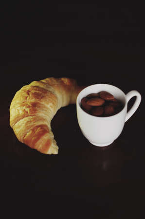 Nuts. White coffee cup with almonds and croissant. Close-upの写真素材