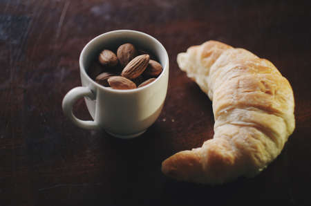 Nuts. White coffee cup with almonds and croissant. Close-upの写真素材