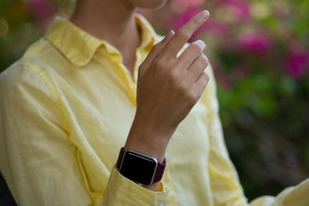 A woman is wearing yellow linen shirt and smartwatch with silicone band. Intelligent fitness watch. Close up. Long slim fingers and neck.の写真素材