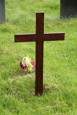 A Simple Wooden Cross with Flowers in a Graveyard 	の写真素材