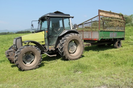 A Tractor with a Grass Collector Trailer at a Farm.