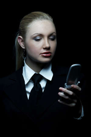 Beautiful business woman wearing black tie and jacket isolated on black background with cell phoneの写真素材