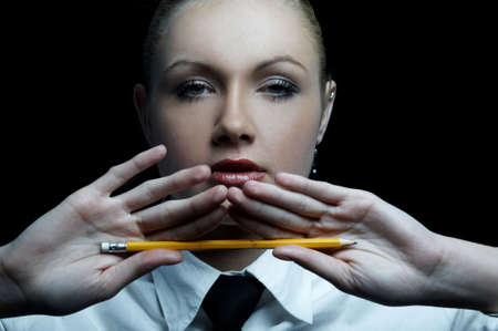 Beautiful business woman wearing black tie and white shirt isolated on black background holding pencilの写真素材