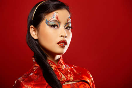 Beautiful Asian girl as a plastic doll on red backgroundの写真素材