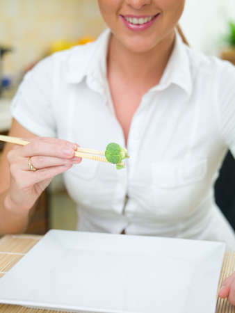Beautiful woman in kitchen eating using chopsticksの写真素材