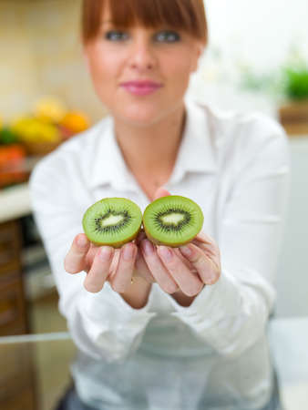 Beautiful woman in kitchen holding kiwi fruitの写真素材