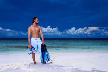Handsome man is standing on the beach holding finの写真素材