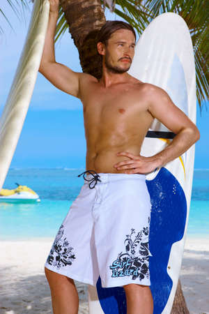 Handsome man standing with surfing board on the beachの写真素材