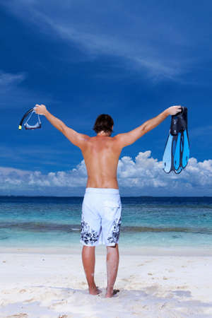 Handsome man is standing on the beach holding finの写真素材