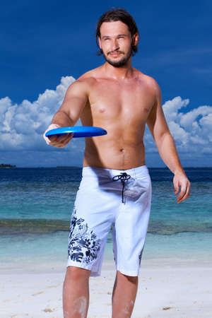 Handsome man is playing on the beach with freesbeeの写真素材