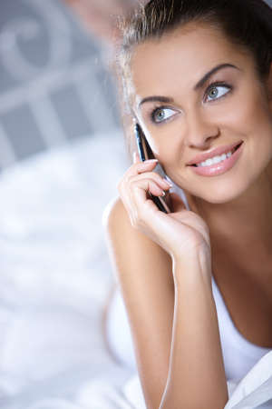 Beautiful woman working on laptop on white bedの写真素材