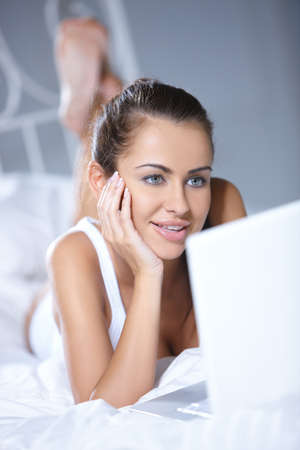 Beautiful woman working on laptop on white bedの写真素材