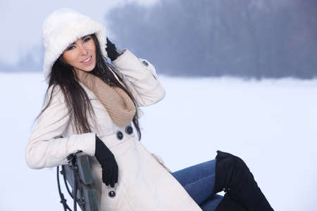 Beautiful and sexy woman sitting on bench in snowy outdoorsの写真素材
