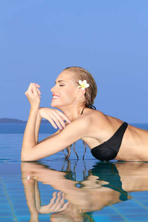 Smiling woman with wet hair laying with her arms on the tiled edge of the pool reflected in the water belowの写真素材