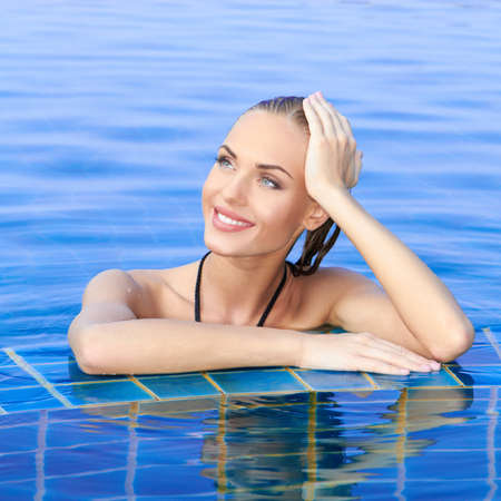 Smiling woman with wet hair standing with her arms on the tiled edge of the pool reflected in the water belowの写真素材