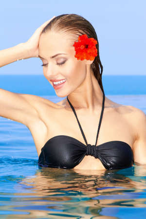 Woman with red flower posing in swimming poolの写真素材