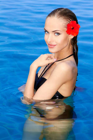 Tropical girl with flower on her ear posing in swimming poolの写真素材