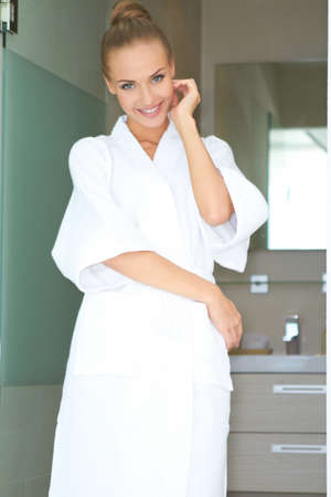 Relaxed woman standing in white bathrobe in modern roomの写真素材