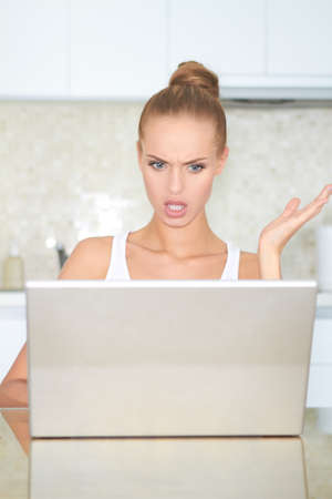 Woman seated at a table looking at her laptop screen in consternation and horrorの写真素材