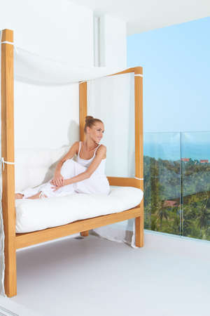 Woman relaxing on a canopied seat on a glass fronted patio overlooking the ocean enjoying tropical luxuryの写真素材