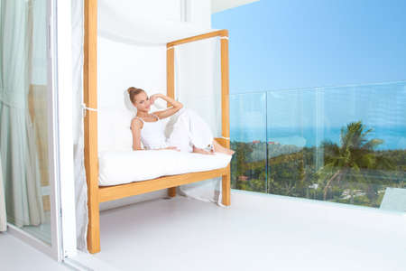 Woman relaxing on a canopied seat on a glass fronted patio overlooking the ocean enjoying tropical luxuryの写真素材