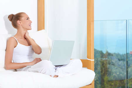 Joyful woman seated on white cushions laughing with with her laptop balanced on her crossed legsの写真素材
