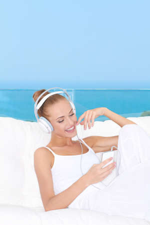 Cute woman wearing headphones relaxing on a white sofa listening to musicの写真素材