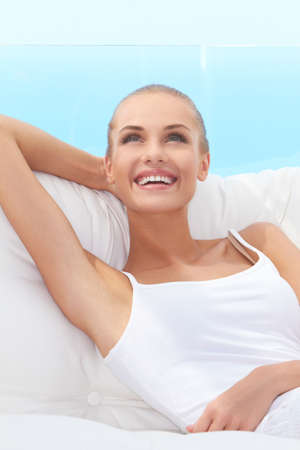 Adorable woman smiling broadly and looking off camera while seated on a white couchの写真素材