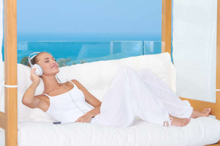 Dreaming woman wearing headphones relaxing on a white sofa listening to musicの写真素材