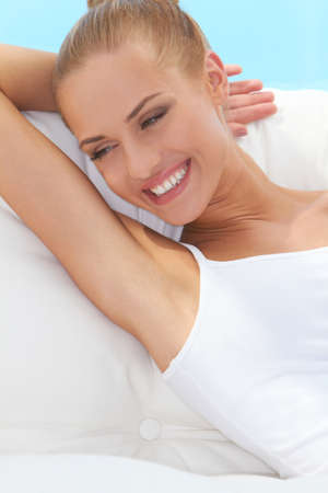 Happy confident beautiful woman smiling broadly and looking off camera while seated on a white couchの写真素材