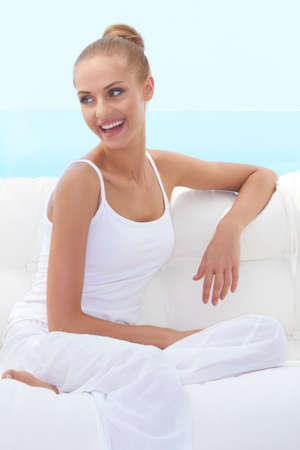 Happy confident beautiful woman smiling broadly and looking off camera while seated on a white couchの写真素材