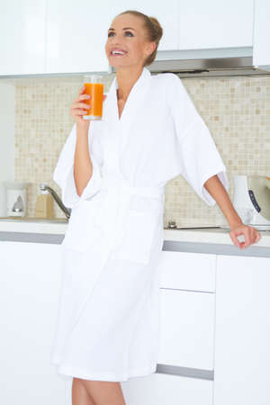 Glamorous woman in a white bath robe enjoying a large glass of fresh orange juice for breakfastの写真素材